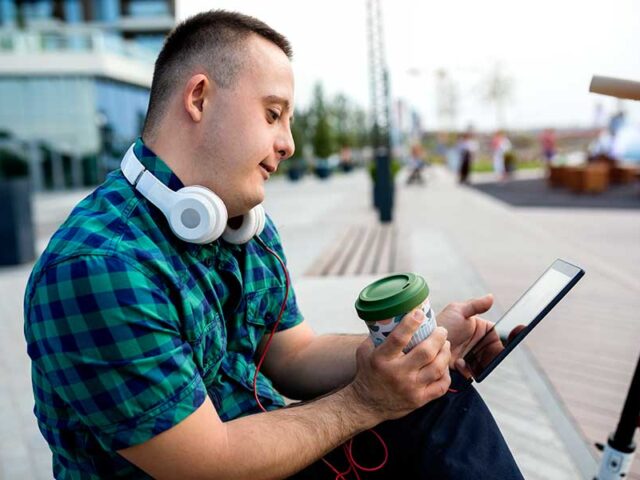 Young man living independently. Drinking coffee and looking at a tablet with headphones attached