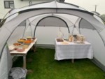 Grey gazebo pitched on grass. Inside it tables of food and drink 