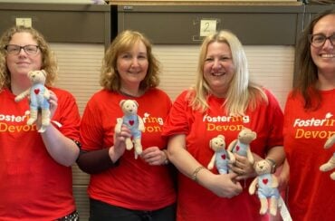 4 x members of the fostering devon team in red branded shirts holding cuddly toy bears