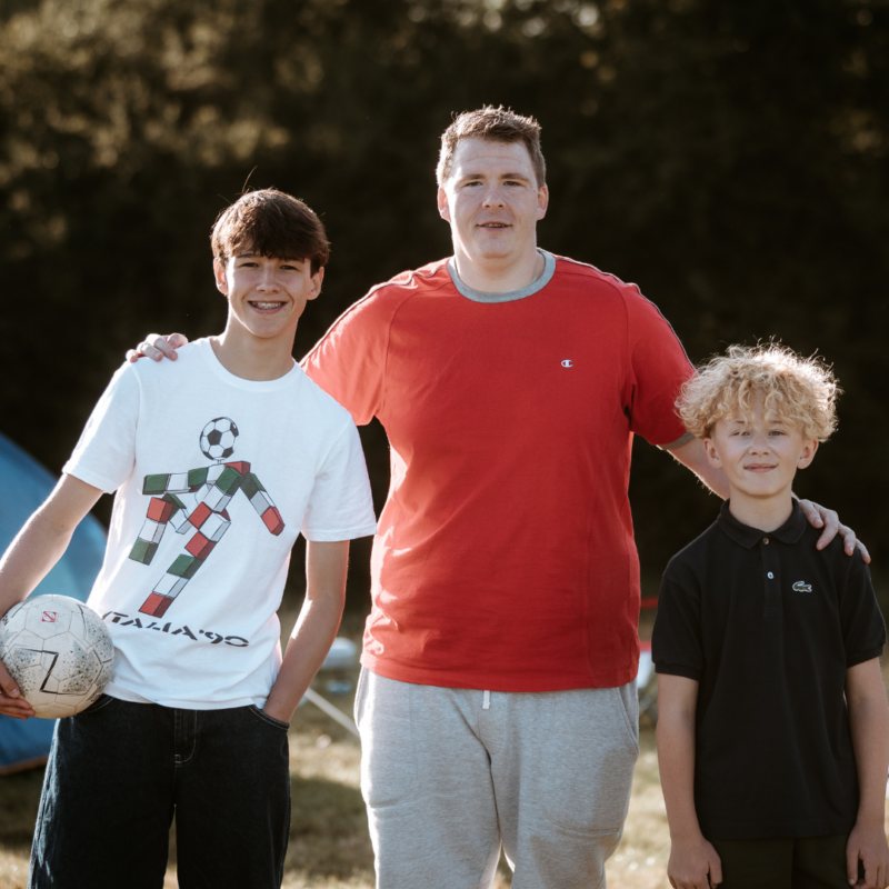 Foster dad stood with arms around 2 foster children. 