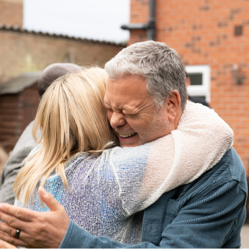 Foster dad stood smiling whilst he hugs a woman with blond hair