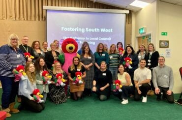 Representatives from local authorities part of the South West recruitment hub stand together for photo in front of screen which says 'Fostering South West - The Gateway to Local Council Fostering'